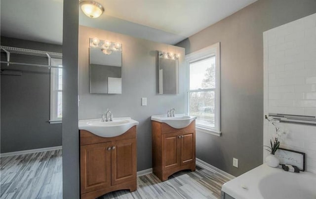 bathroom featuring wood finished floors, two vanities, baseboards, and a sink