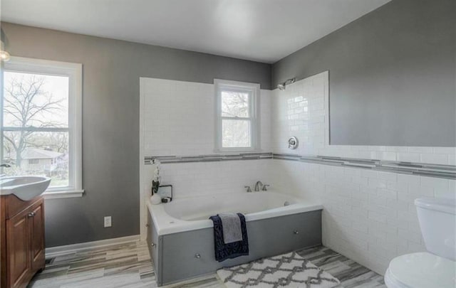 bathroom featuring a garden tub, toilet, a healthy amount of sunlight, and tile walls