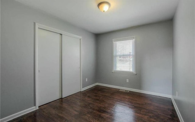 unfurnished bedroom with a closet, visible vents, baseboards, and wood finished floors