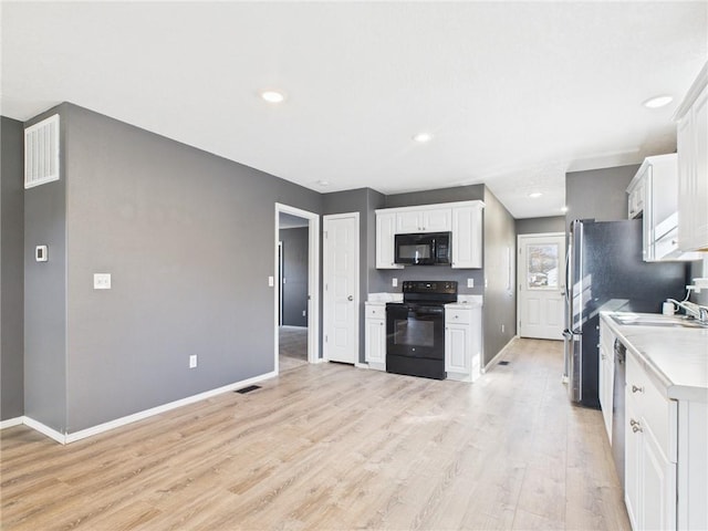 kitchen with visible vents, light wood finished floors, black appliances, white cabinets, and light countertops