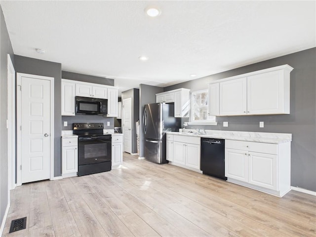 kitchen featuring visible vents, black appliances, white cabinetry, light wood finished floors, and baseboards