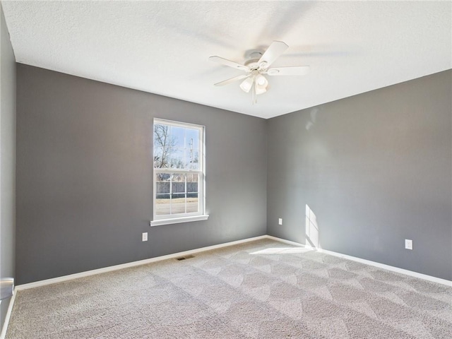 carpeted empty room with visible vents, a textured ceiling, baseboards, and ceiling fan