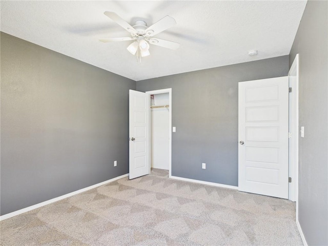 unfurnished bedroom with ceiling fan, baseboards, light carpet, a closet, and a textured ceiling