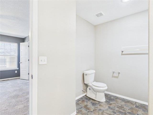 bathroom featuring a textured ceiling, baseboards, visible vents, stone finish flooring, and toilet