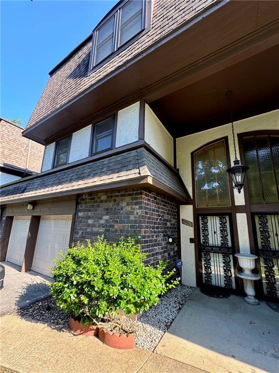 entrance to property featuring stucco siding, an attached garage, brick siding, and a shingled roof