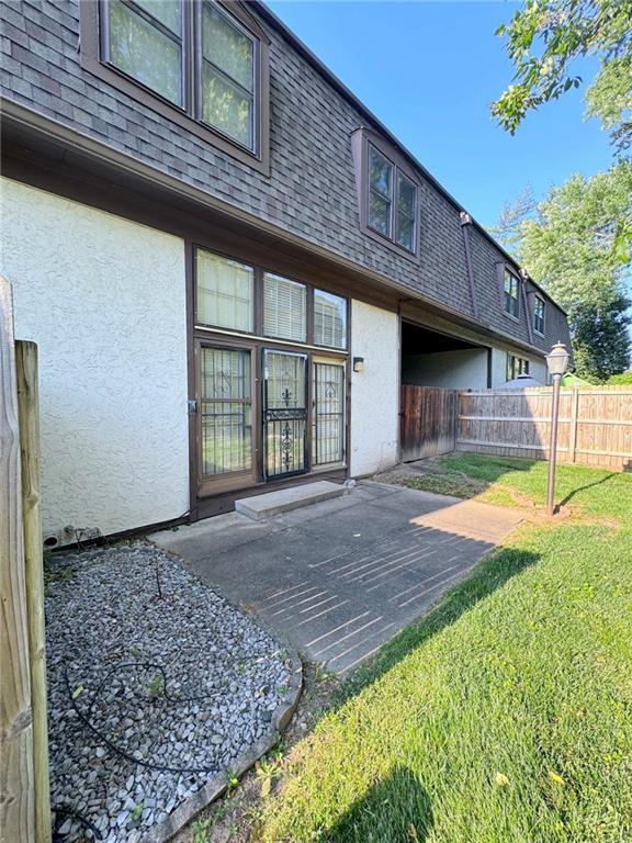 rear view of property with mansard roof, fence, roof with shingles, and stucco siding