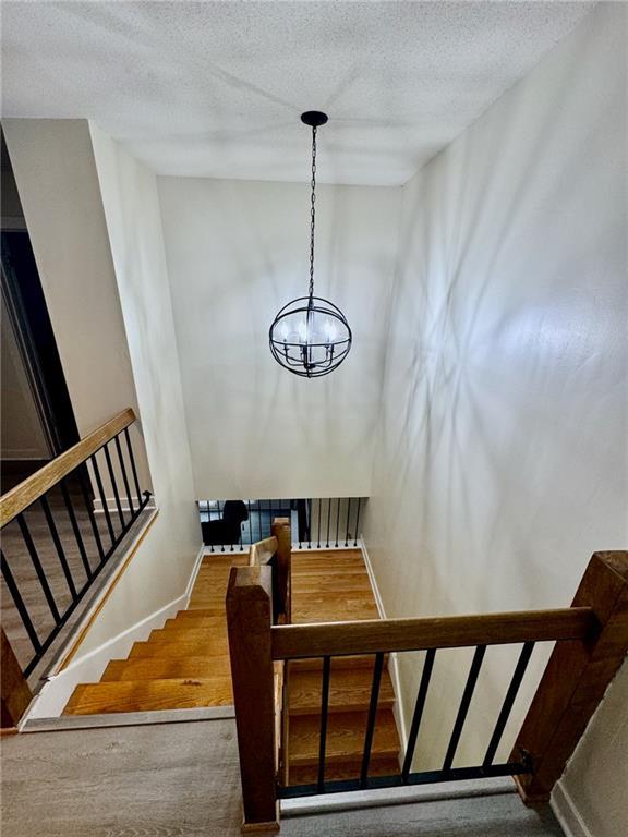 staircase with a chandelier, a textured ceiling, and baseboards