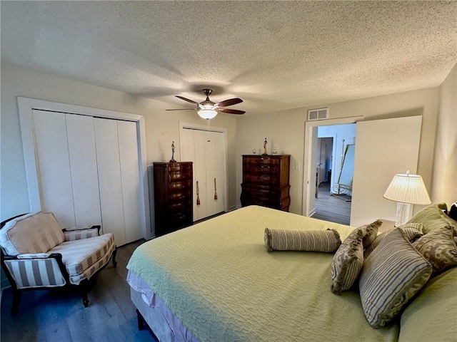 bedroom featuring wood finished floors, visible vents, ceiling fan, multiple closets, and a textured ceiling