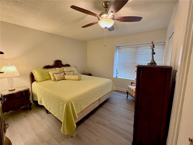 bedroom with ceiling fan, wood finished floors, baseboards, and a textured ceiling