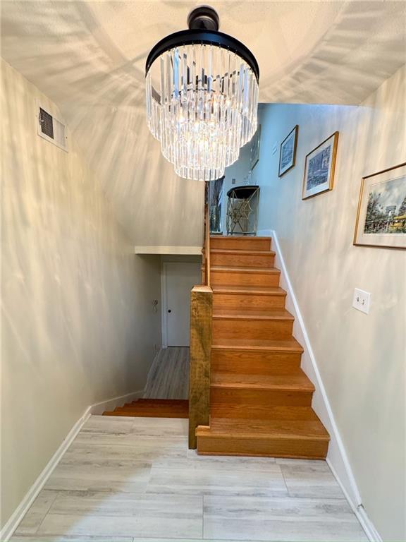 stairway with visible vents, baseboards, an inviting chandelier, and wood finished floors