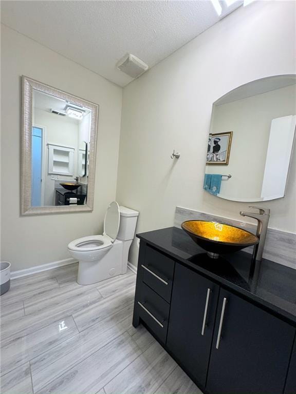 bathroom featuring baseboards, toilet, vanity, wood finished floors, and a textured ceiling