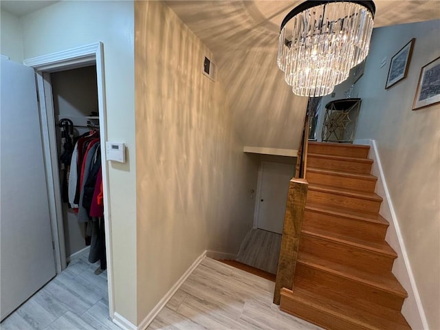 stairs with an inviting chandelier, wood finished floors, and baseboards