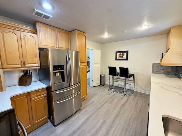 kitchen with light wood-style flooring, visible vents, stainless steel fridge, and light countertops