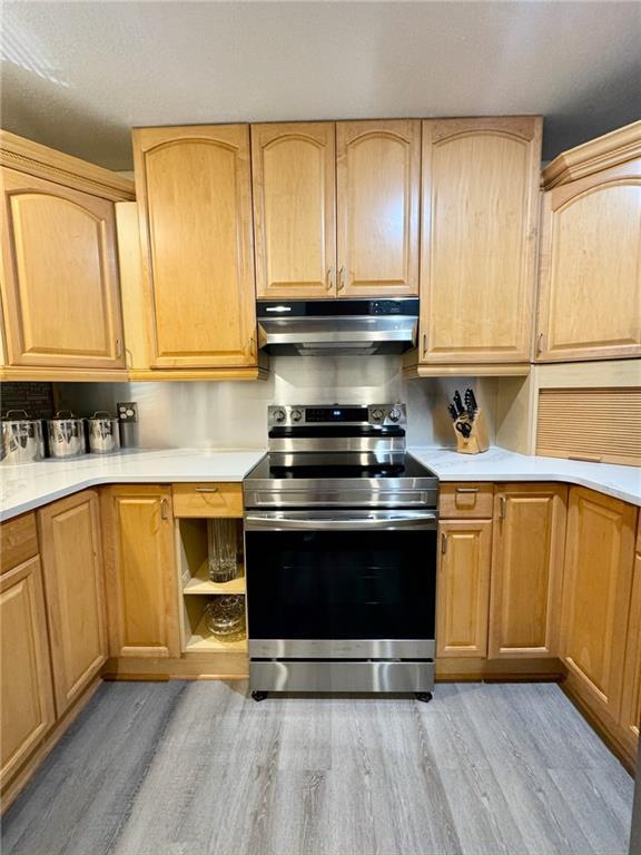 kitchen featuring light brown cabinets, electric stove, under cabinet range hood, light wood-style floors, and light countertops