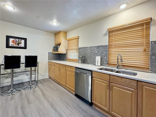 kitchen with a sink, backsplash, light wood-style floors, appliances with stainless steel finishes, and light countertops