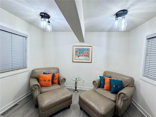 living area with wood finished floors, beamed ceiling, baseboards, and visible vents