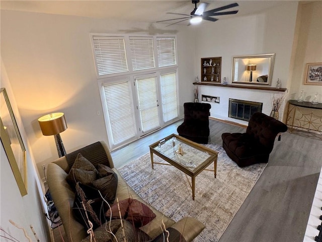 living room featuring a glass covered fireplace, wood finished floors, a towering ceiling, and ceiling fan