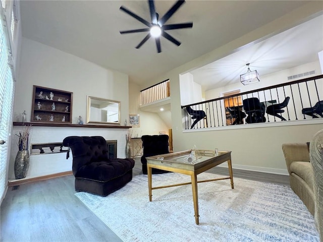 living room with a ceiling fan, wood finished floors, visible vents, baseboards, and a glass covered fireplace