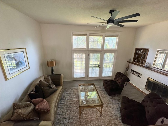 living area with wood finished floors, baseboards, a fireplace, ceiling fan, and a textured ceiling