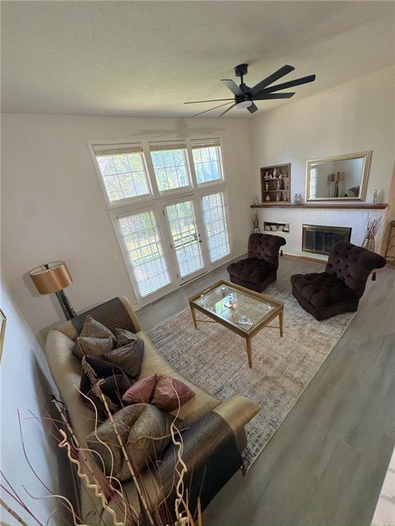 living area featuring a glass covered fireplace, a textured ceiling, ceiling fan, and wood finished floors