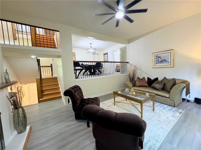 living area with baseboards, wood finished floors, stairs, and ceiling fan with notable chandelier