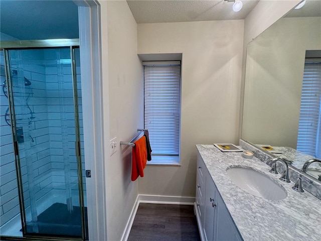 bathroom with baseboards, vanity, a stall shower, wood finished floors, and a textured ceiling