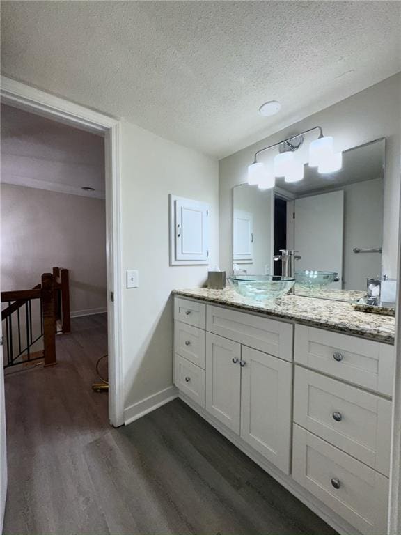 bathroom with a textured ceiling, vanity, baseboards, and wood finished floors