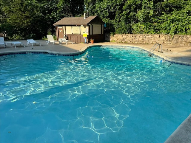 pool featuring an outdoor structure, a patio area, fence, and an exterior structure