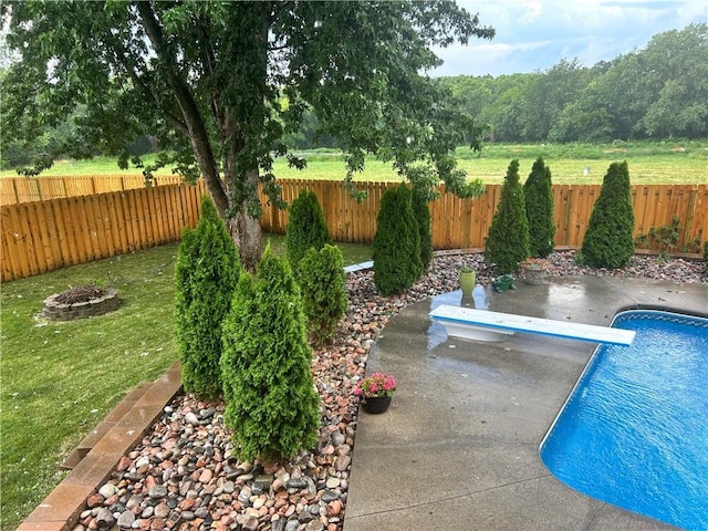 view of swimming pool featuring a fenced backyard, a diving board, a fire pit, a patio area, and a lawn