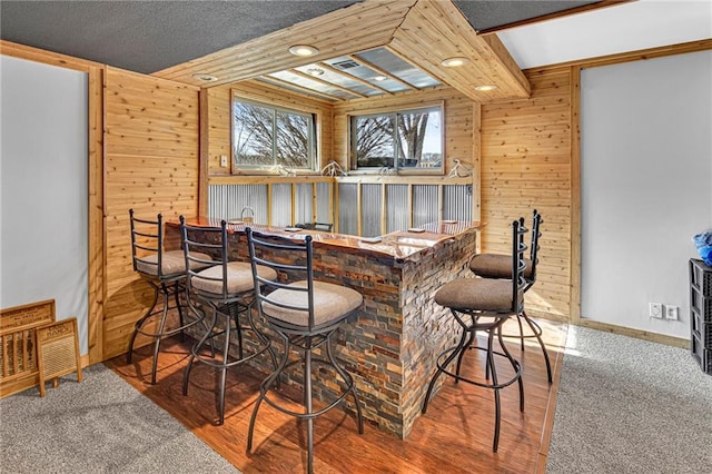 bar with wooden walls, baseboards, indoor bar, beam ceiling, and wood finished floors