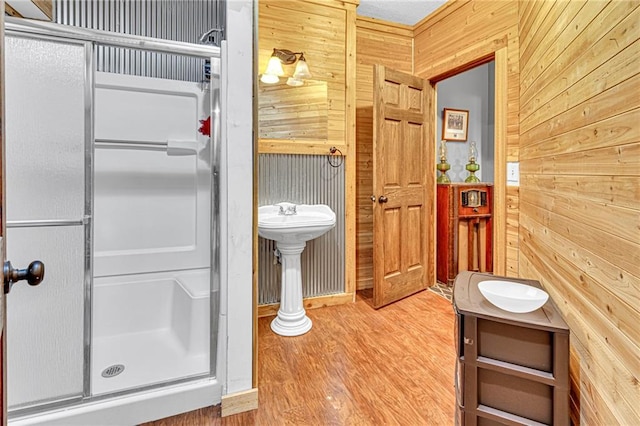 bathroom featuring wooden walls, wood finished floors, a stall shower, and a sink