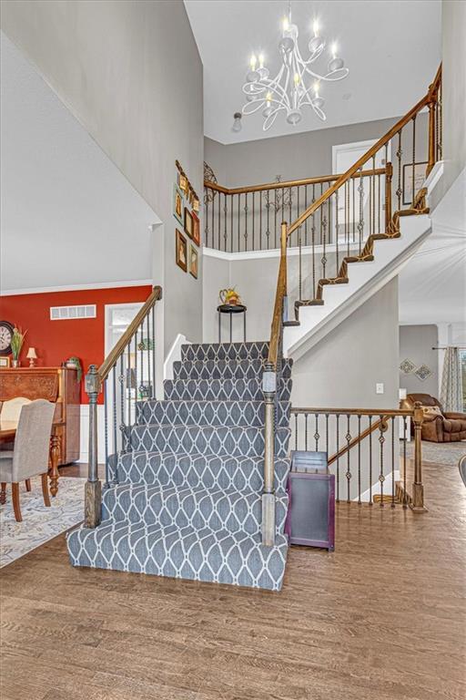 stairway featuring visible vents, an inviting chandelier, wood finished floors, and a towering ceiling