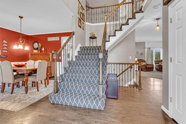 stairway with visible vents, baseboards, ornamental molding, an inviting chandelier, and wood finished floors