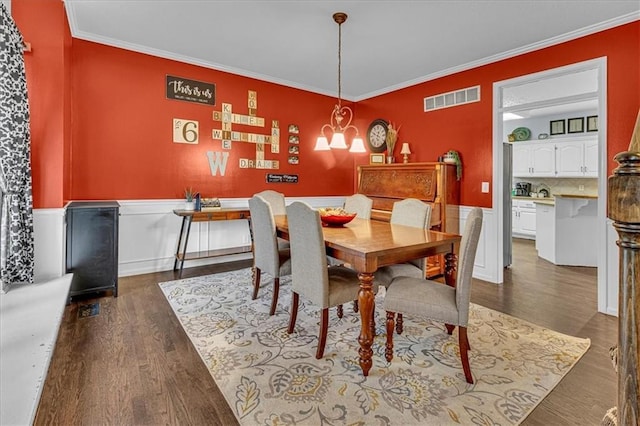 dining space with dark wood finished floors, an inviting chandelier, visible vents, and ornamental molding