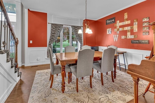 dining space featuring stairway, wood finished floors, an inviting chandelier, crown molding, and a decorative wall