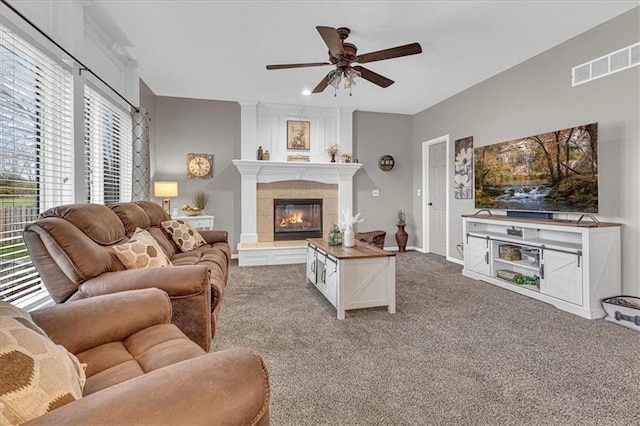 living room featuring a ceiling fan, baseboards, visible vents, a tile fireplace, and light colored carpet