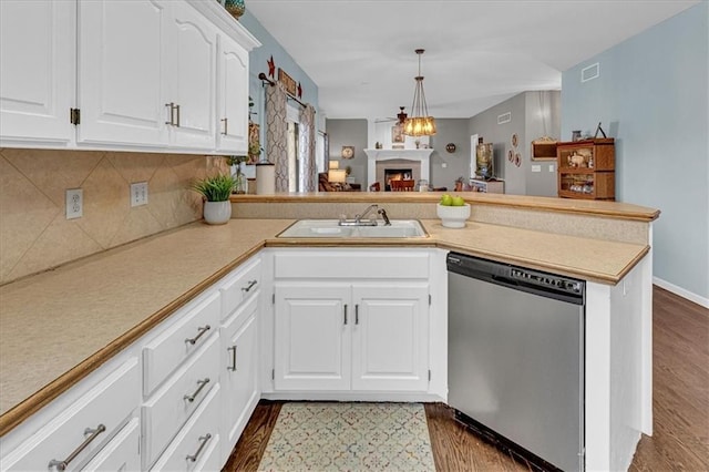 kitchen featuring a sink, a warm lit fireplace, a peninsula, light countertops, and dishwasher