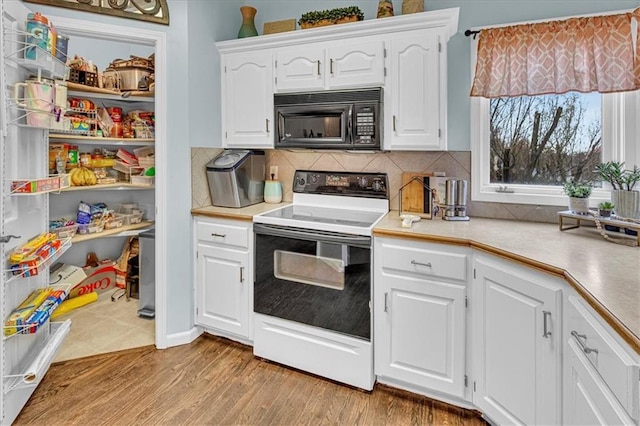 kitchen with black microwave, light countertops, electric stove, light wood-style floors, and white cabinets