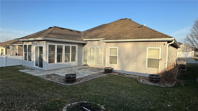 rear view of property with fence, roof with shingles, a lawn, a sunroom, and a patio area