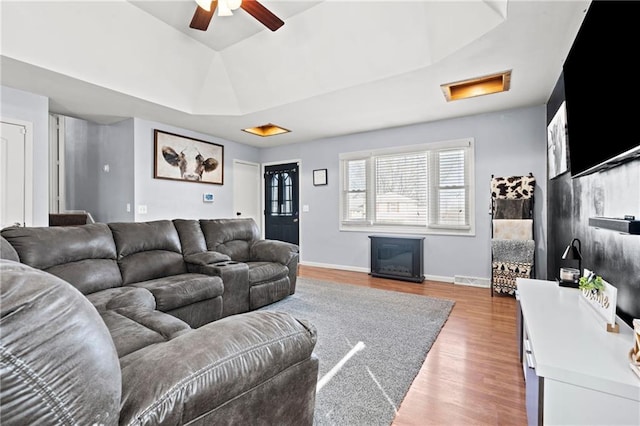 living area with a tray ceiling, wood finished floors, a glass covered fireplace, baseboards, and attic access