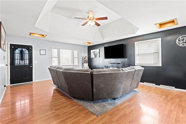 living area featuring visible vents, baseboards, attic access, light wood-style flooring, and a raised ceiling