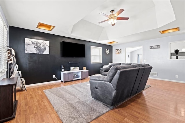 living area featuring visible vents, a raised ceiling, light wood-style flooring, baseboards, and attic access