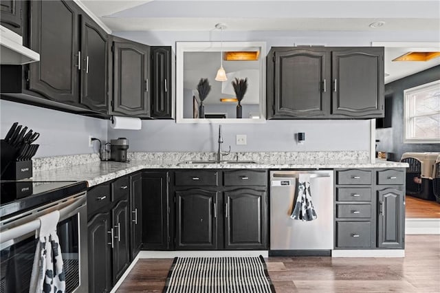 kitchen featuring a sink, light wood-style floors, under cabinet range hood, appliances with stainless steel finishes, and dark cabinets