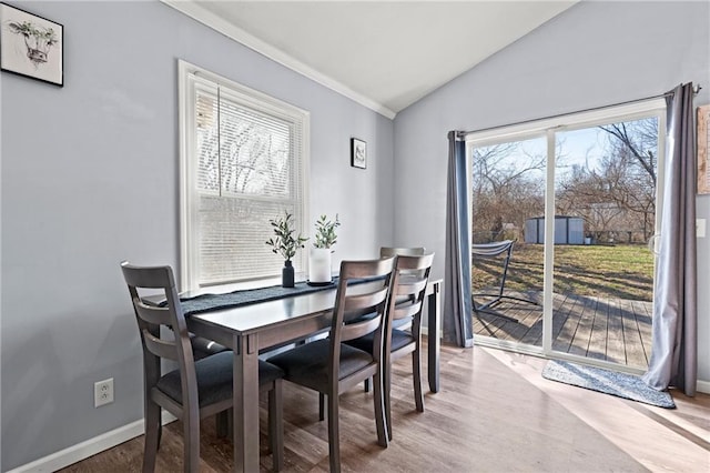 dining space featuring baseboards, wood finished floors, ornamental molding, and vaulted ceiling