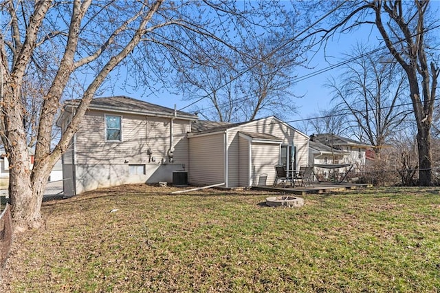 back of property featuring a fire pit, fence, a wooden deck, central AC unit, and a lawn