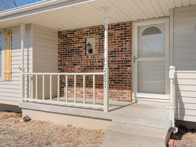 view of exterior entry with brick siding and a porch