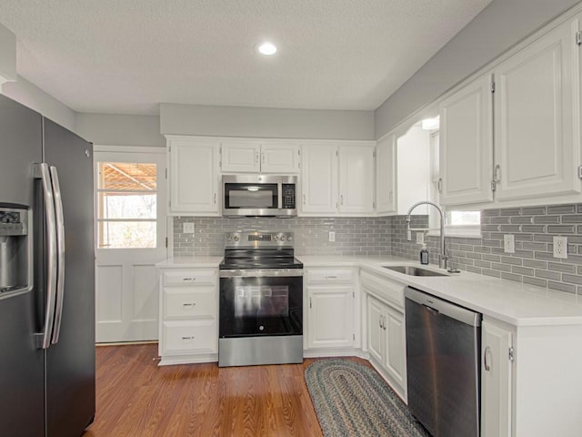 kitchen with light countertops, stainless steel appliances, wood finished floors, white cabinetry, and a sink