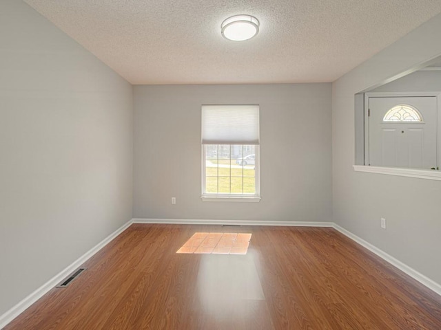 unfurnished room featuring a textured ceiling, wood finished floors, visible vents, and baseboards