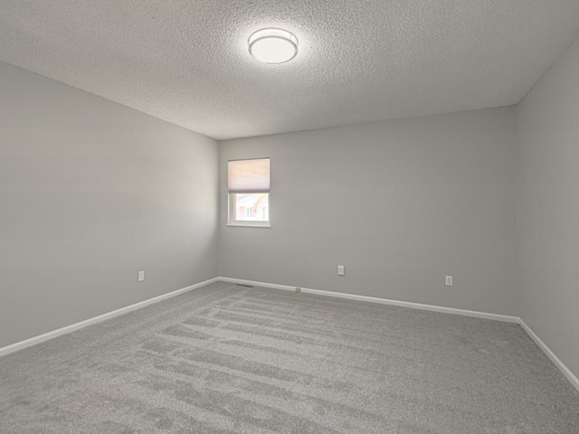 carpeted empty room with a textured ceiling and baseboards