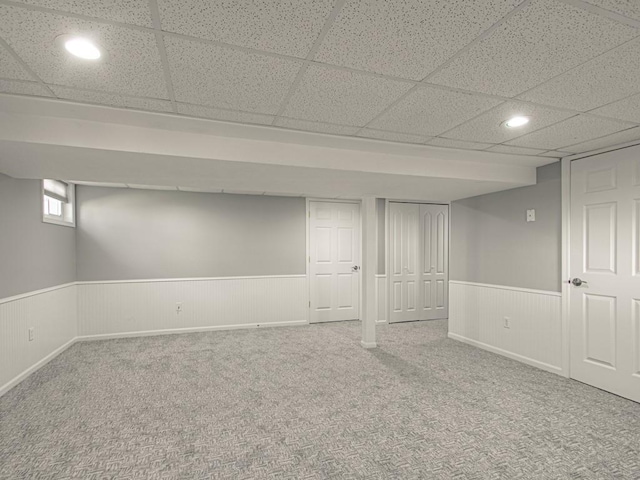 below grade area featuring carpet flooring, a paneled ceiling, recessed lighting, and wainscoting